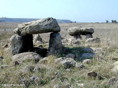 A rocky field with two rudimentary structures made with large stacked stones in an arched shape