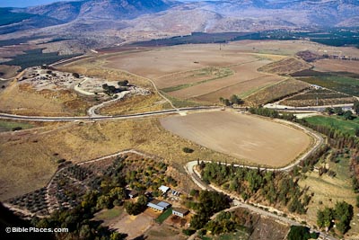 View from airplane of a wide brown valley with roads dividing fields, there are some modern buildings in the foreground