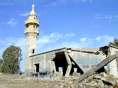 A half demolished, graffitied, cement building with a single tower on one end that has two railed balconies